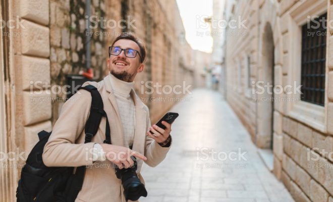 Young male tourist visiting old town Dubrovnik, Croatia. He is holding his phone and camera.